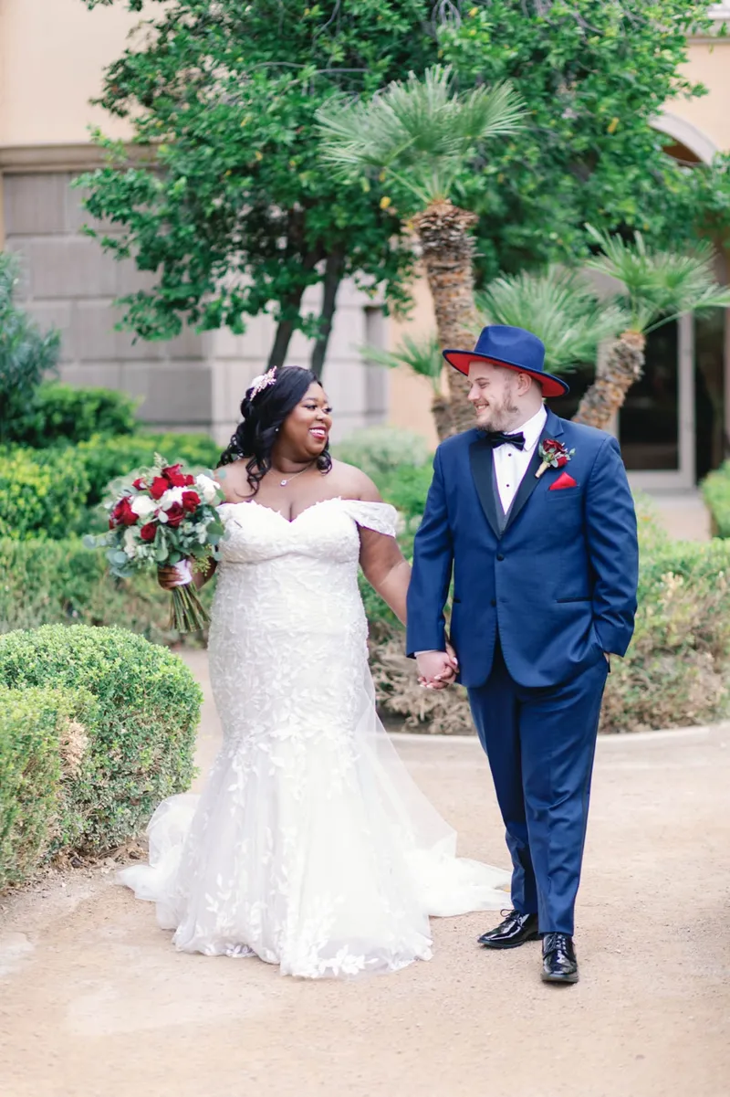 Bride and groom walking hand in hand past boxwood hedges and palms in the courtyard