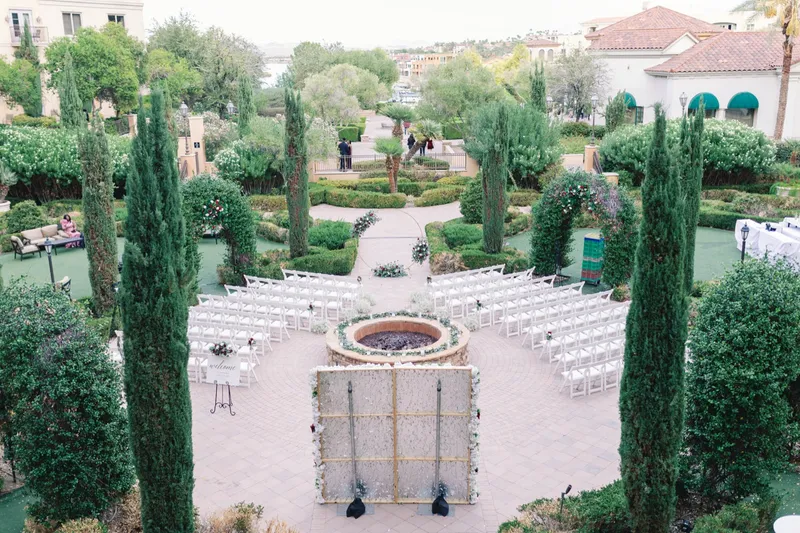 Empty ceremony set from above, rows of white chairs curved around a round stone fire feature ringed with greenery