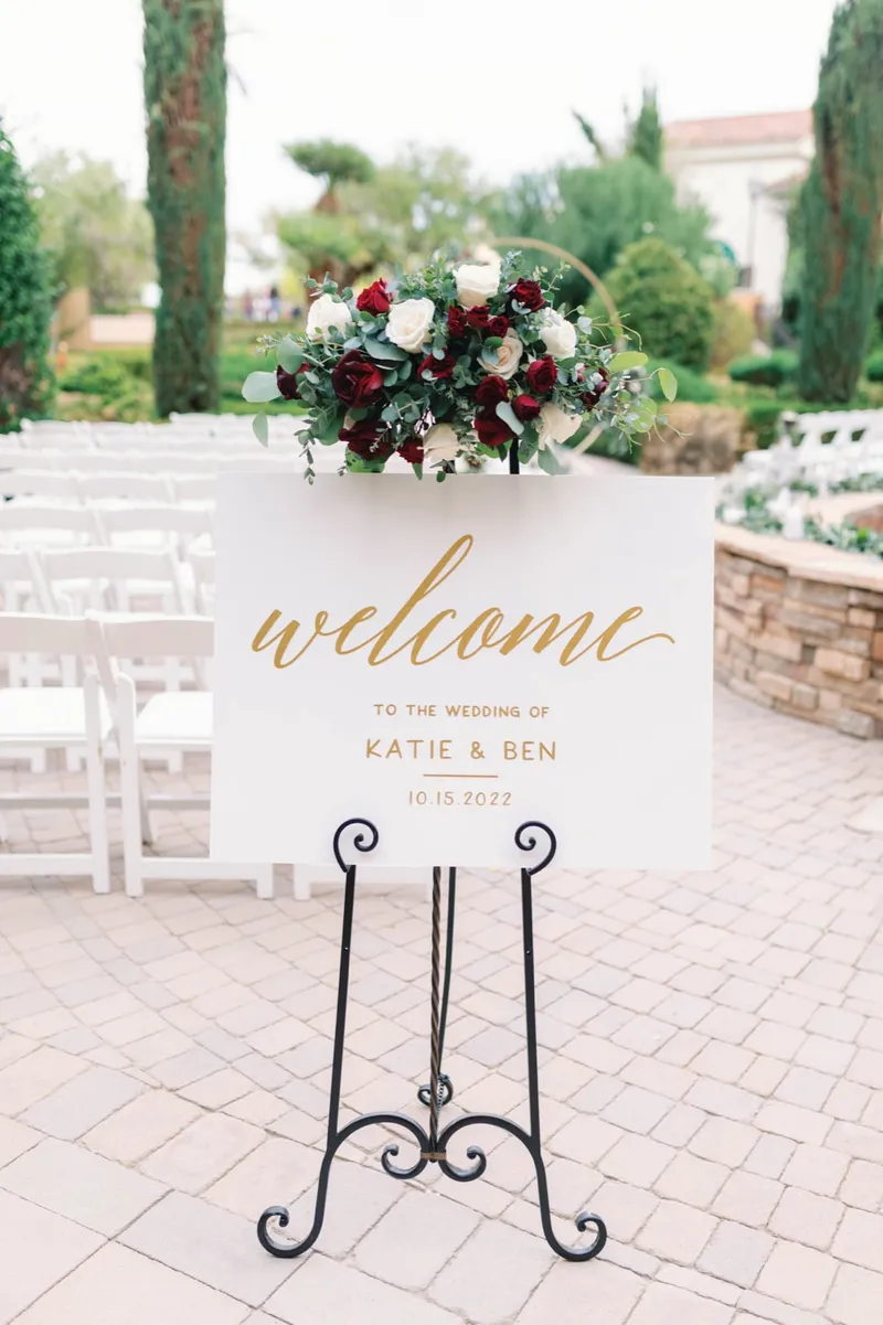 Welcome sign on an iron easel topped with a spray of red and white flowers at the entrance to the garden
