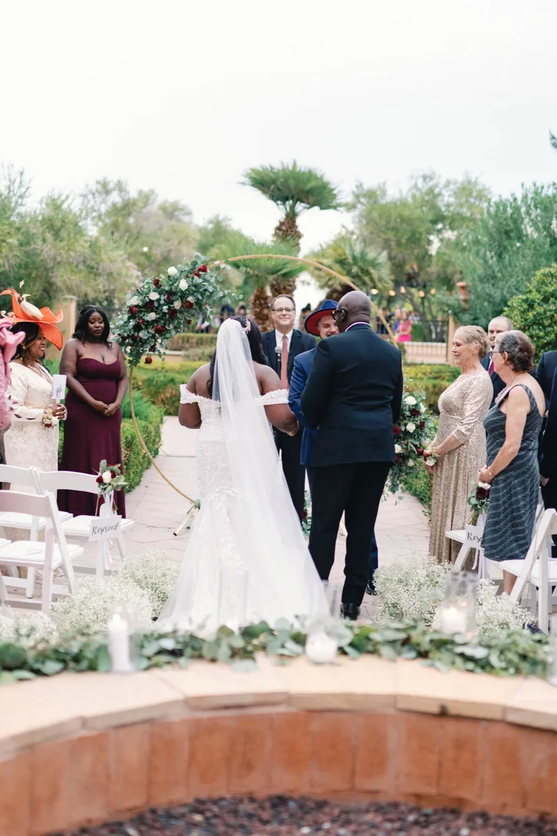 Couple standing at a circular floral arch with guests seated on both sides of the fire feature