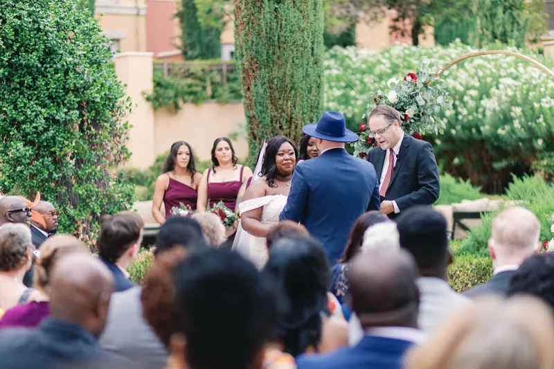Ceremony seen over the heads of seated guests, bridesmaids in burgundy standing along the aisle
