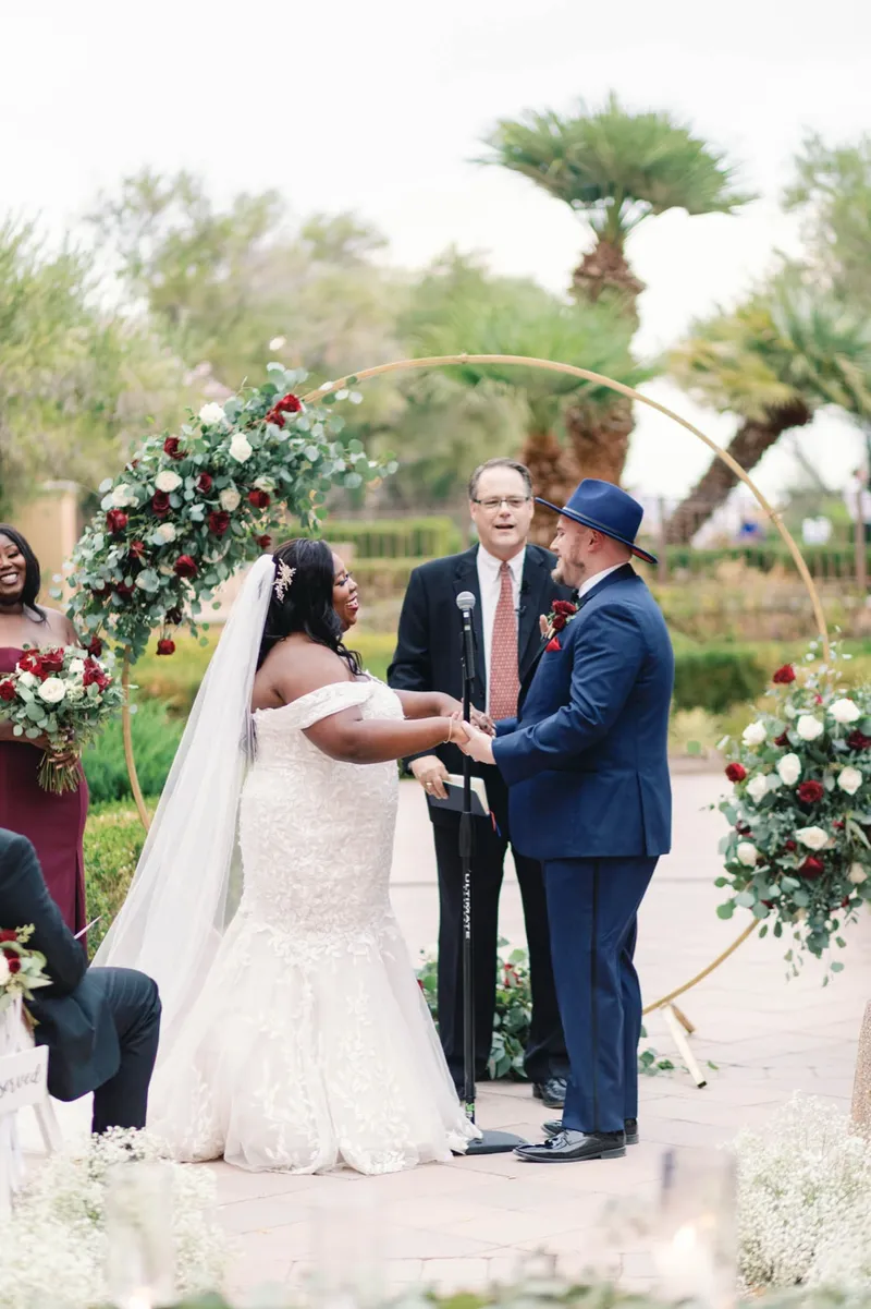 Couple holding hands at the arch while the officiant speaks into a microphone