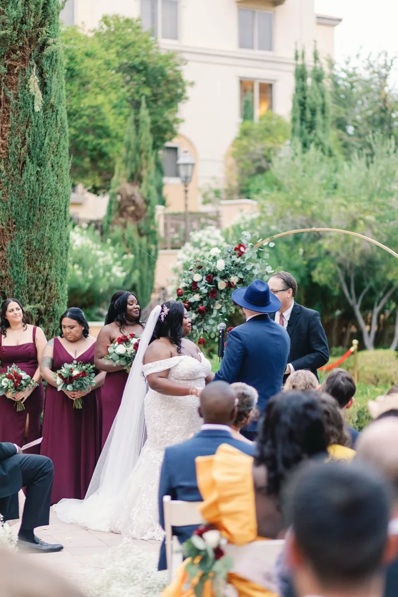 The couple at the arch with the bridesmaids lined up in burgundy to one side