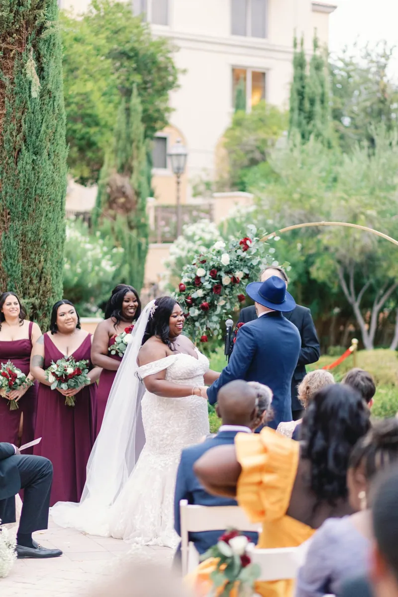 Bride and groom facing each other under the greenery of the arch with the bridal party behind