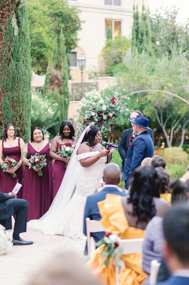 Ring exchange at the floral arch, the bride's hand out and the bridal party watching