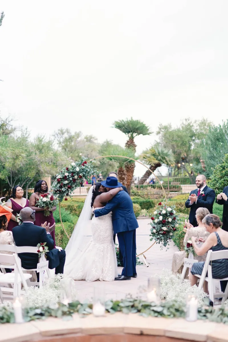 First kiss at the arch as the guests rise from their chairs around the fire feature