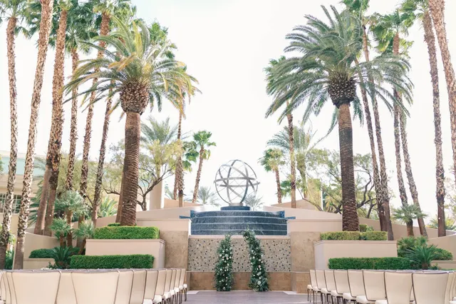 Rows of chairs facing a floral arch set in front of a tiered waterfall, tall palms standing on both sides of the terrace