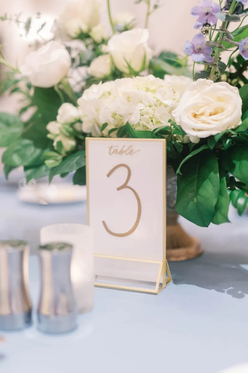 Table number three beside a white and lavender centerpiece and two lit candles
