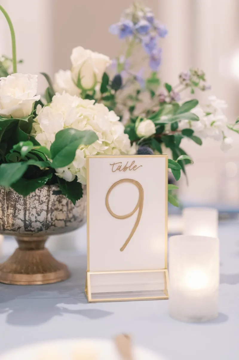 Table number nine next to a footed vase of white blooms and a lit candle