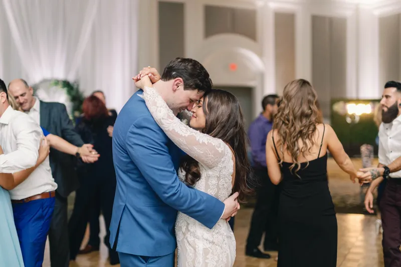 Bride and groom forehead to forehead during a slow dance while guests dance around them