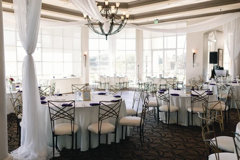 Ballroom set in white linens with navy napkins and gold rimmed chairs, white drapery wrapped around a column and swagged to the chandelier