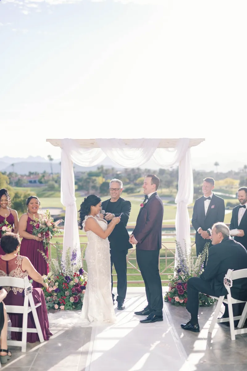 Bride and groom facing each other during the vows, bridesmaids in burgundy standing to the left