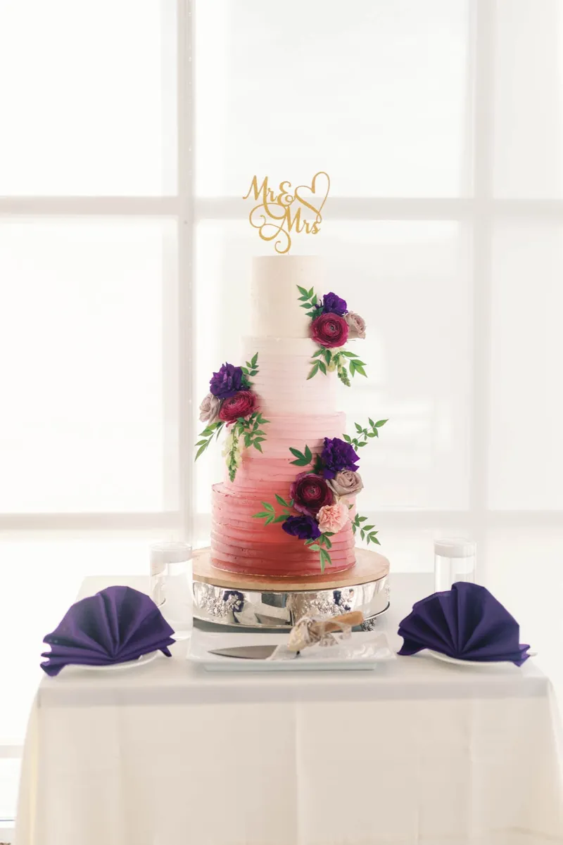 Ombre coral wedding cake trimmed with burgundy and blush flowers under a gold script topper