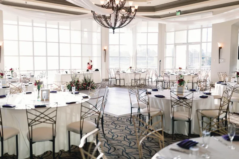 Ballroom with an open dance floor under the chandelier, the cake and the sweetheart table set against the tall windows