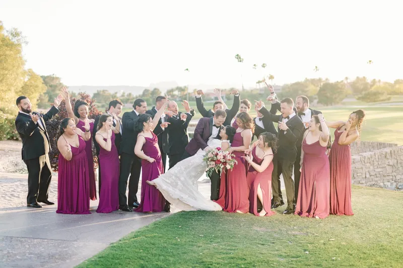 Wedding party cheering on the lawn as the bride swings her skirt out, the course behind them