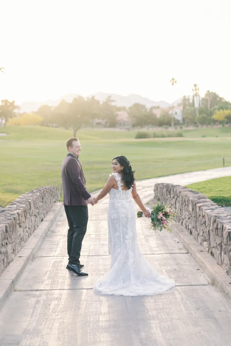 Bride and groom facing each other holding hands on the cart bridge with low sun behind them