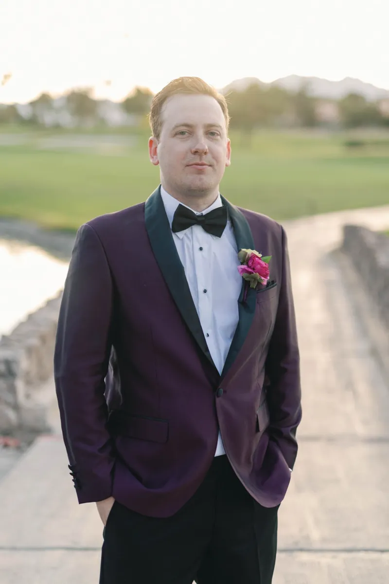 Groom on the bridge in a burgundy tuxedo with a black bow tie and a magenta boutonniere
