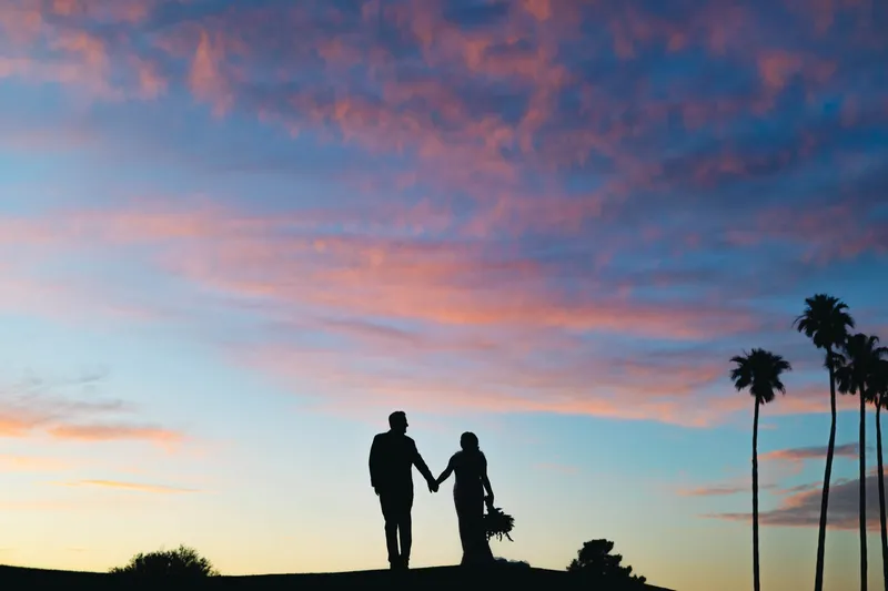 Couple silhouetted hand in hand on the crest of a fairway against a pink and blue sunset sky