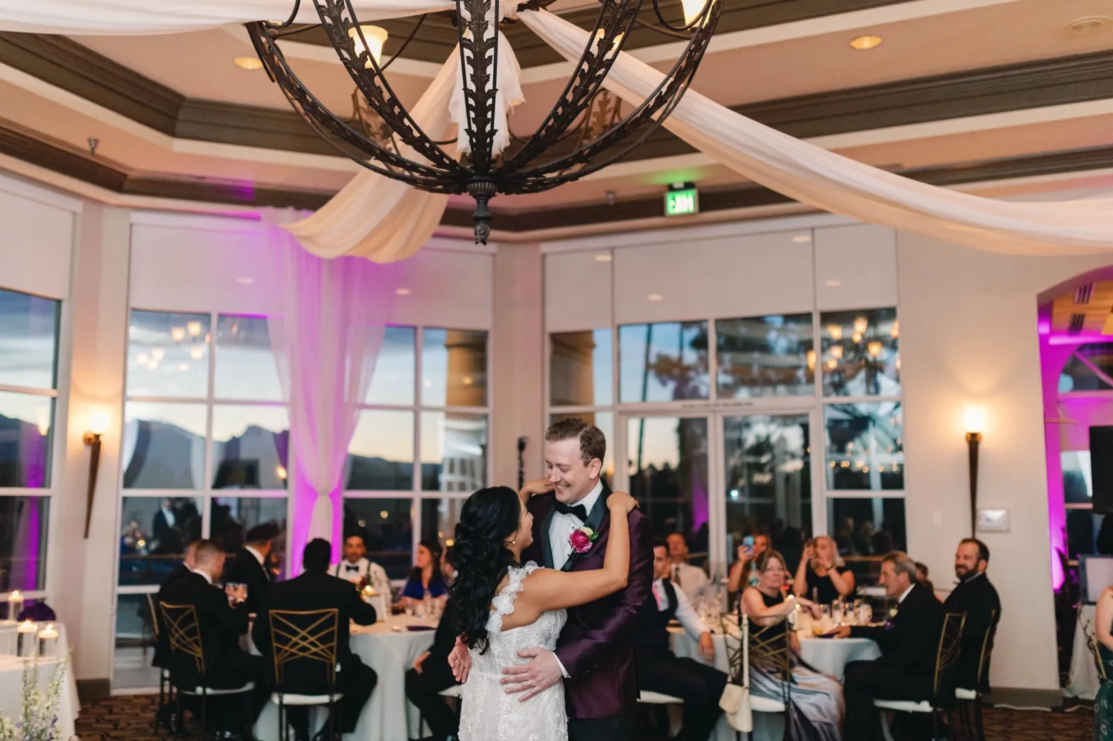 Couple’s first dance on the ballroom floor under the chandelier as guests watch from the tables
