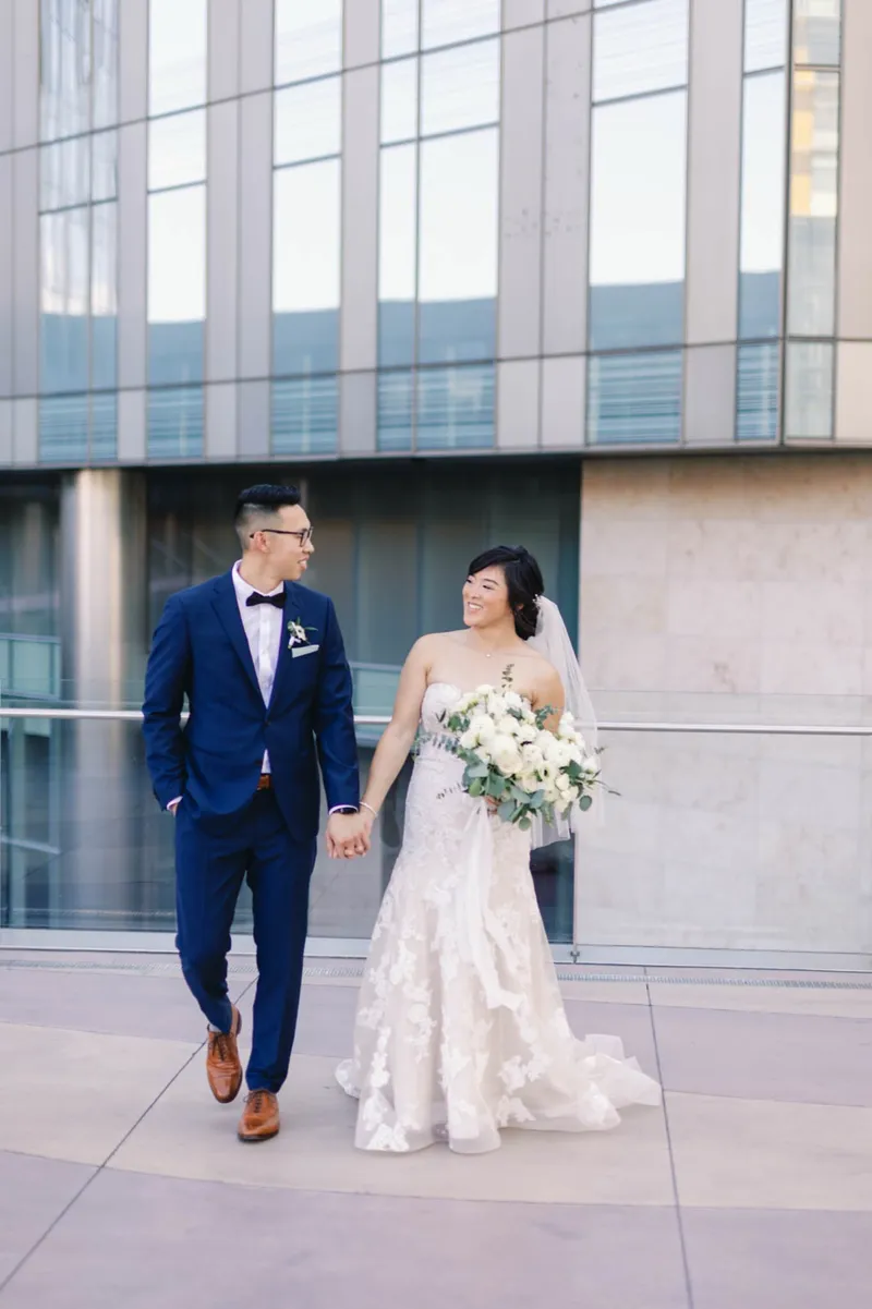 Bride and groom walking hand in hand past the tall windows of the resort