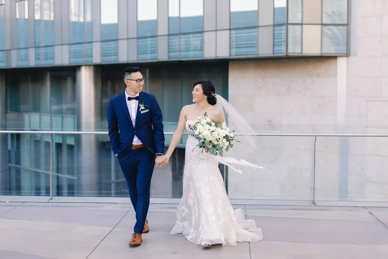 Bride and groom laughing as they walk together, her veil lifting behind her