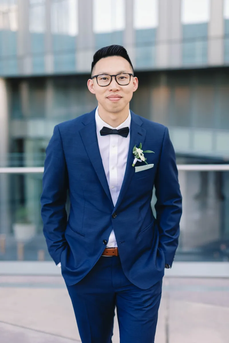 Groom standing for a portrait in a navy suit and black bow tie with a white boutonniere