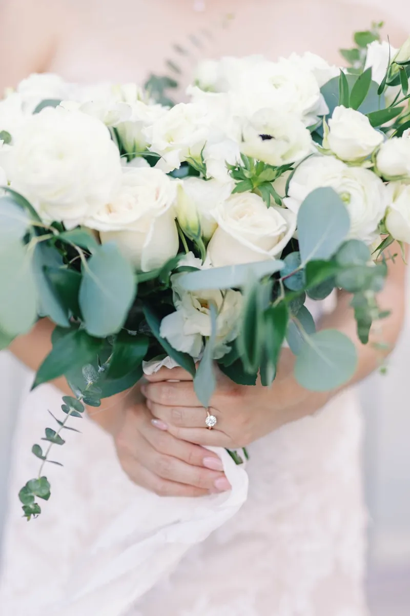 Bride's hand and ring resting on a bouquet of white roses and eucalyptus