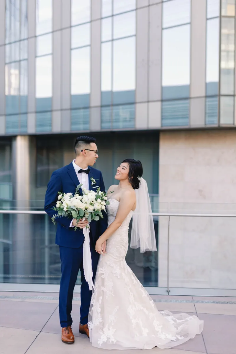 Bride and groom standing together outside looking at each other, her bouquet held between them