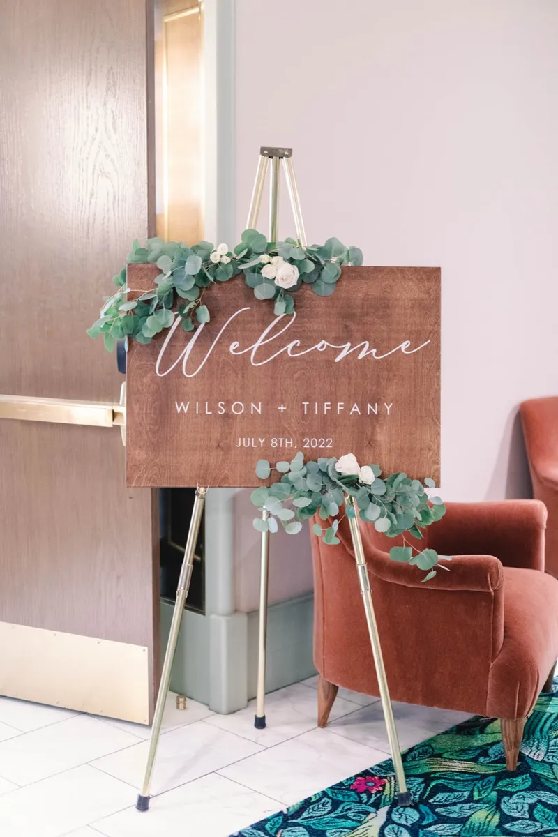 Wooden welcome sign on an easel with the couple's names, dressed with eucalyptus and white blooms