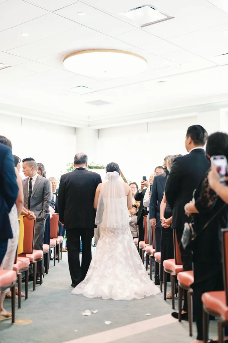 Bride walking up the aisle on her father's arm as the seated guests stand and turn to watch