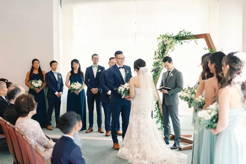 Full wedding party lined up on both sides of the greenery arch during the ceremony