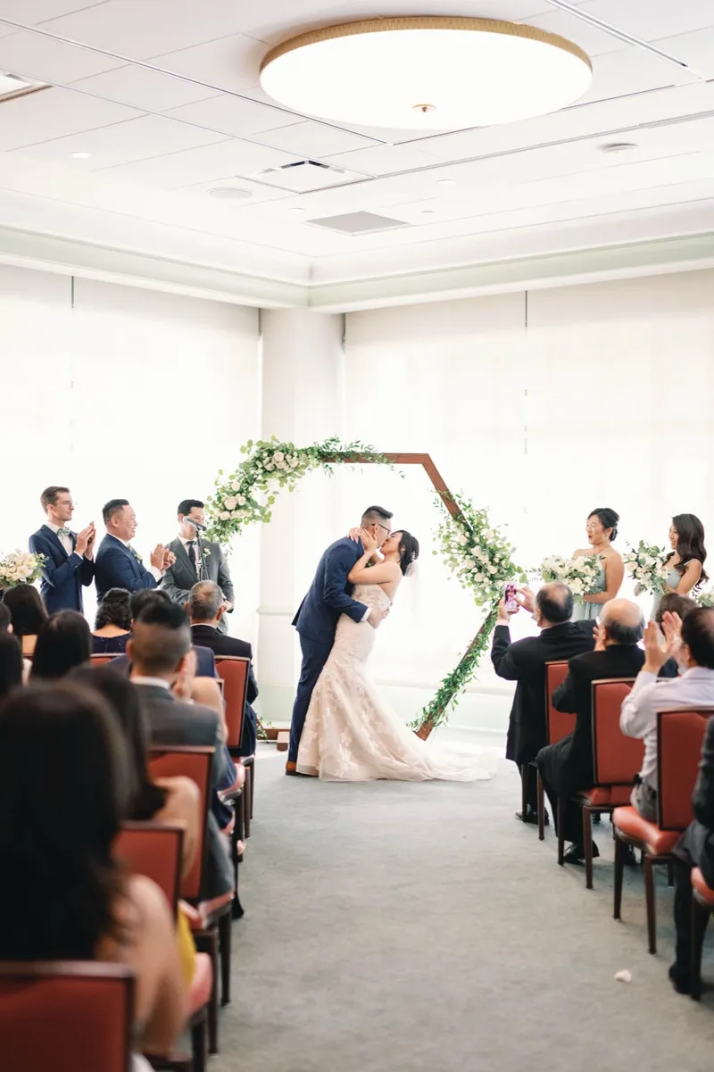 First kiss at the greenery arch while the guests applaud