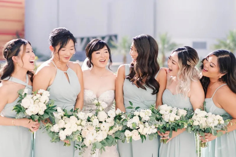Bride laughing in a line with her bridesmaids, all of them holding white bouquets