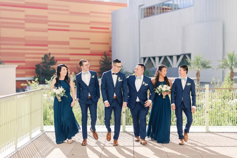 Wedding party walking the terrace together in navy suits and sage green dresses