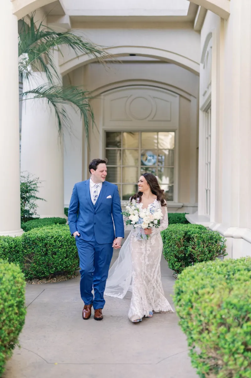 Bride and groom walking hand in hand down the garden path toward the camera