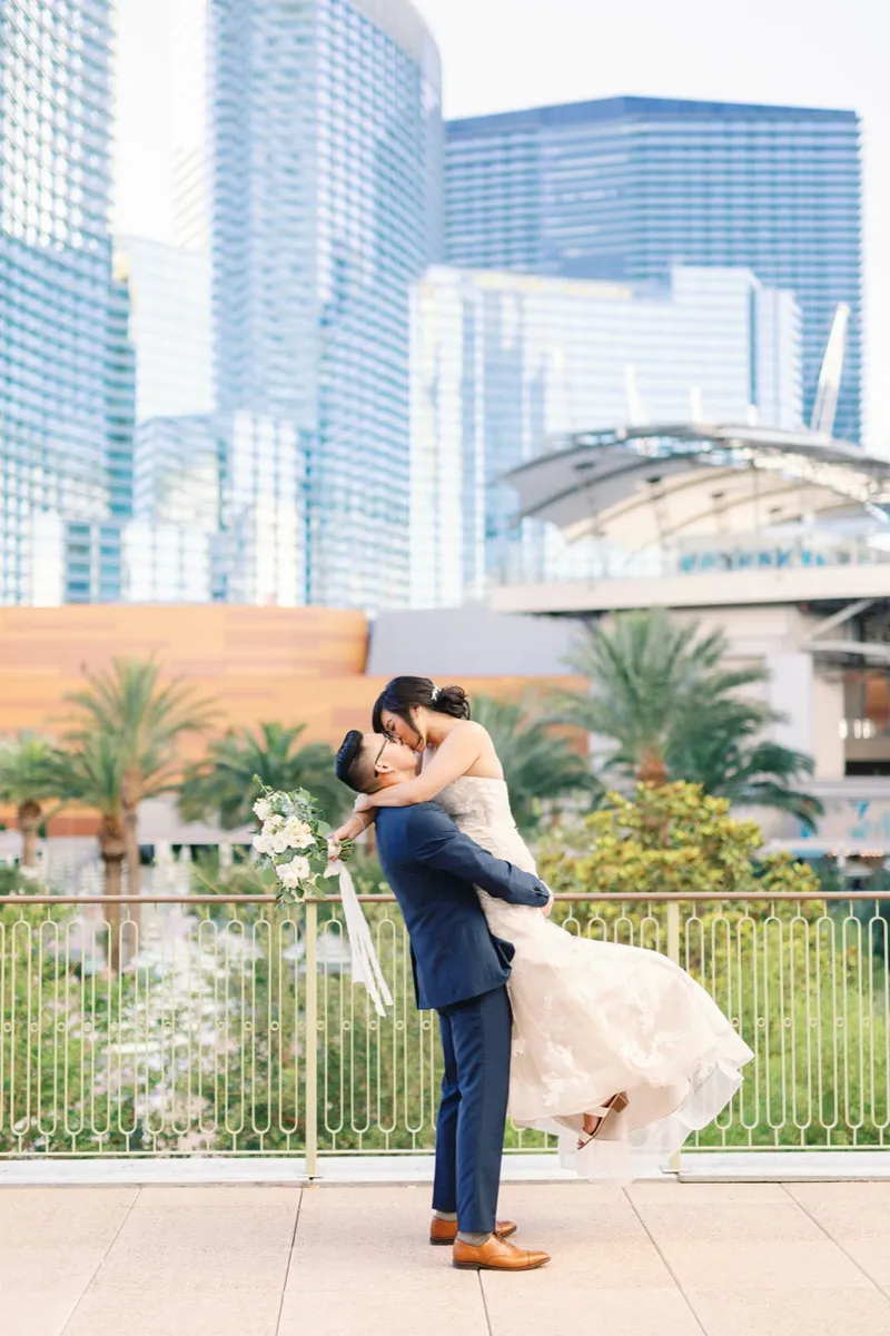 Groom lifting the bride as her gown swings out, palms and glass towers behind