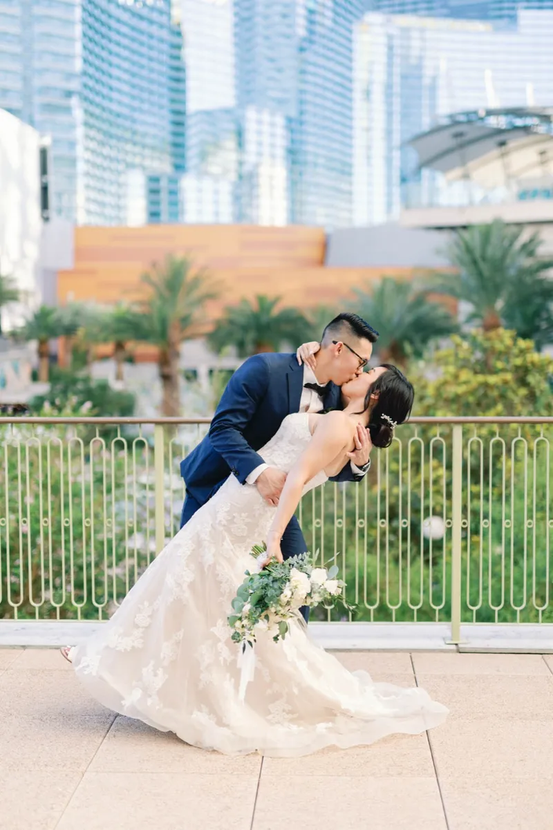 Groom dipping the bride into a kiss at the terrace railing with the Strip behind them