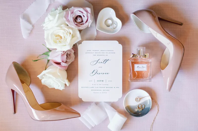 The same invitation styled with nude heels, a perfume bottle, a ring dish and cream roses