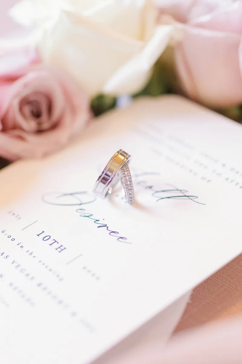 Close view of a diamond ring resting on the corner of the invitation beside a blush rose