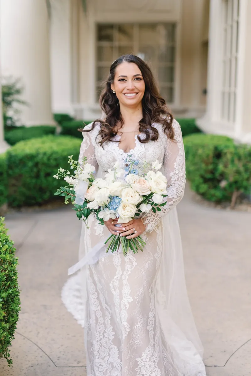 Bride smiling on the garden walkway holding her white and blue bouquet