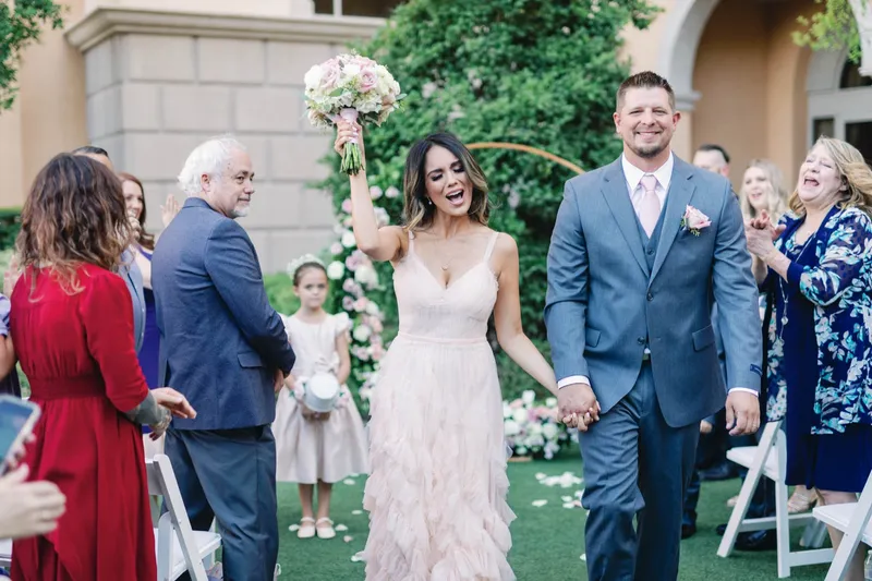 Bride raising her bouquet overhead as the couple walk out through their guests