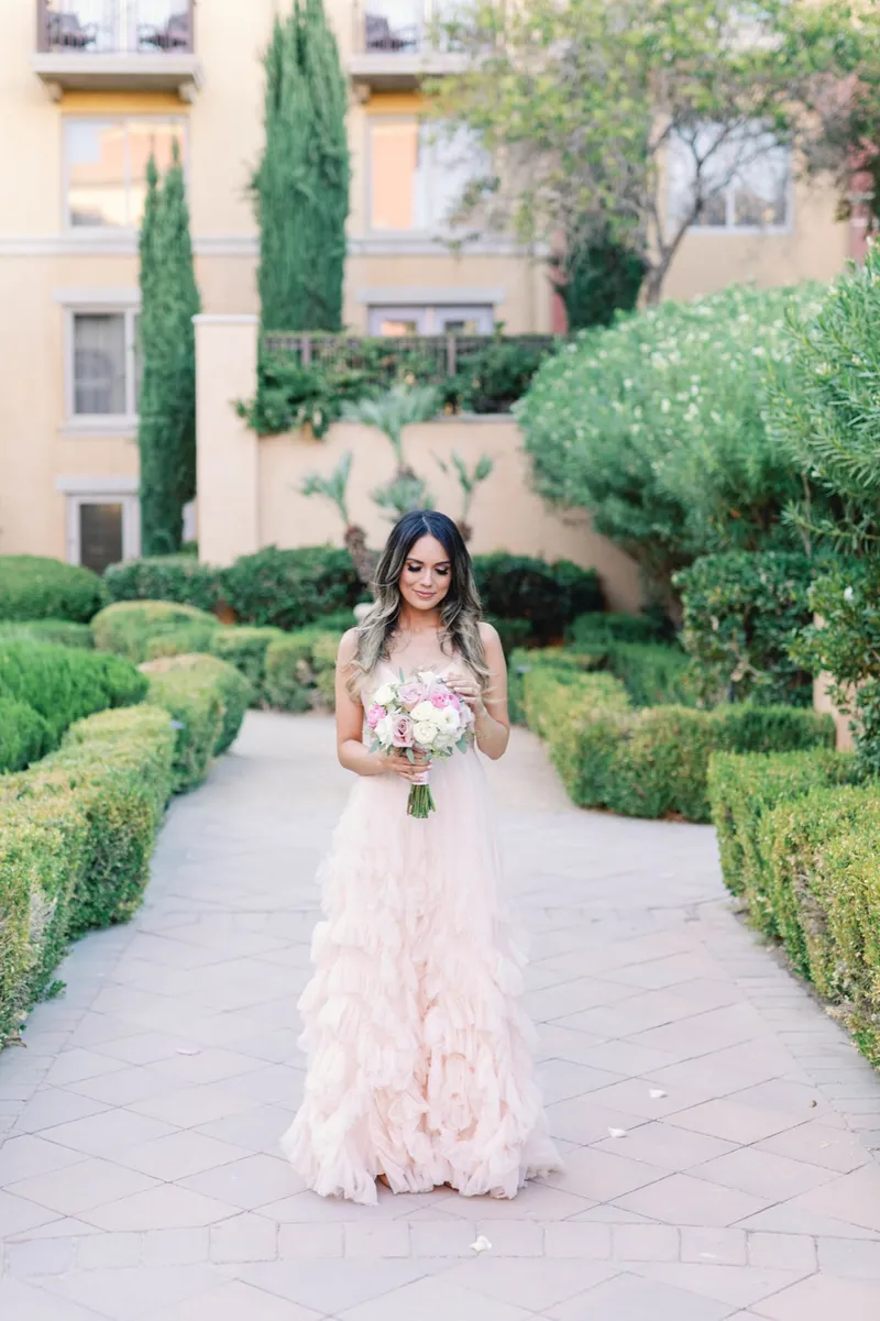 Bride standing alone on a boxwood lined path holding her pink and white bouquet