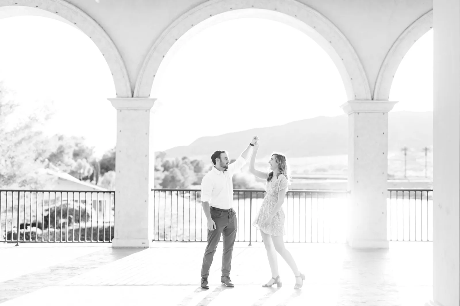 Black and white photo of a man spinning his partner under his arm on a terrace of tall stone arches above the lake