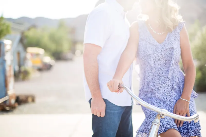 Close backlit frame of the couple with their hands together on the bicycle handlebars, the sun flaring between them