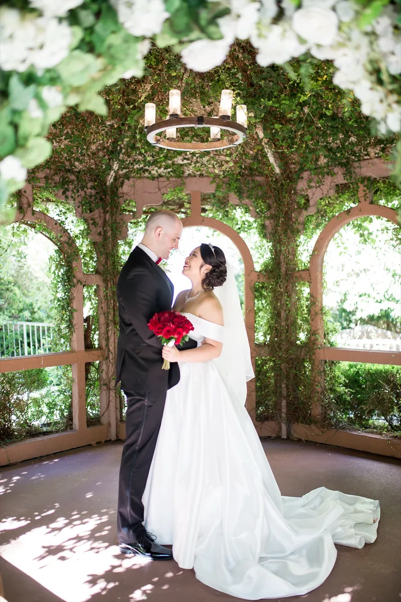 Bride and groom holding each other inside the gazebo, dappled light falling across the floor