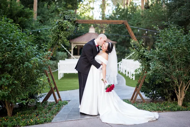 Groom dipping the bride into a kiss on the garden path with the ivy covered gazebo and rows of white chairs behind them