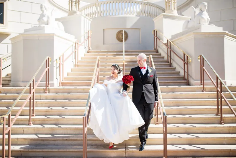 Bride and groom coming down a wide stone staircase flanked by white sphinx statues, the bride carrying her skirt