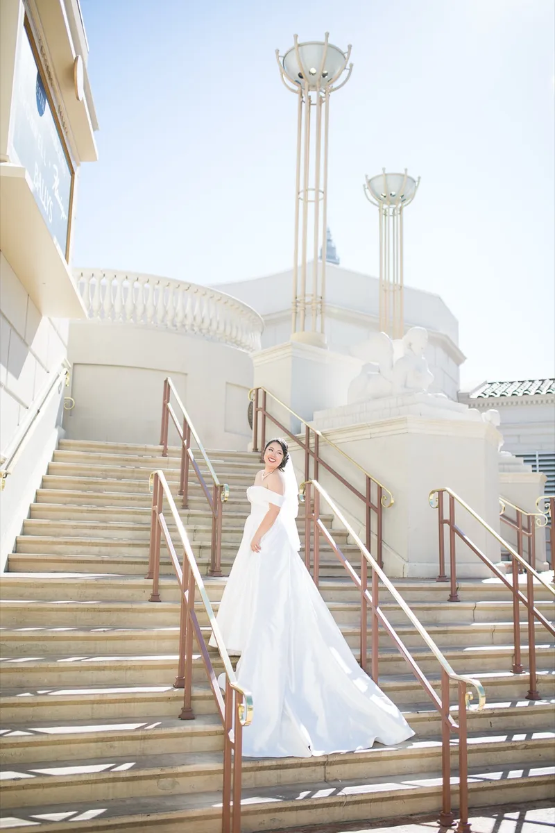 Bride alone on the stone staircase looking back over her shoulder with her train spread behind her