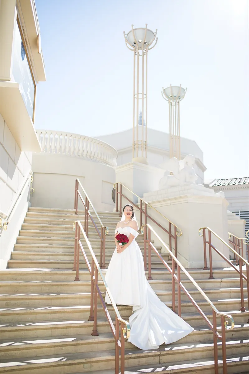 Bride standing centered on the wide staircase with her red rose bouquet and her full satin skirt
