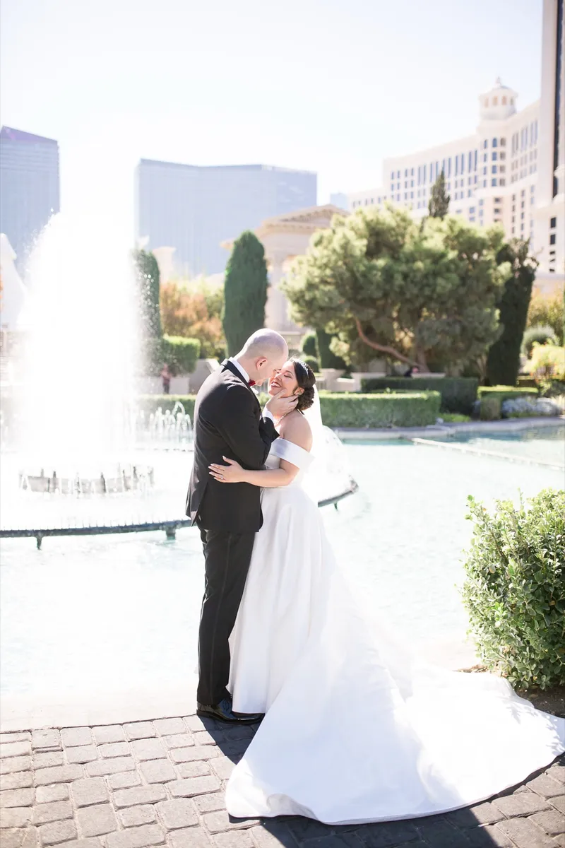 Bride and groom laughing in each other's arms in front of a resort fountain with glass towers behind